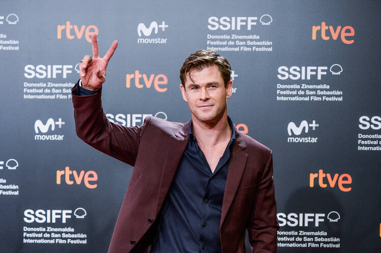 Chris Hemsworth wearing a maroon suit and giving the peace sign