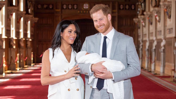 Prince Harry Wearing a Suit With Meghan Markle in White Holding the Baby
