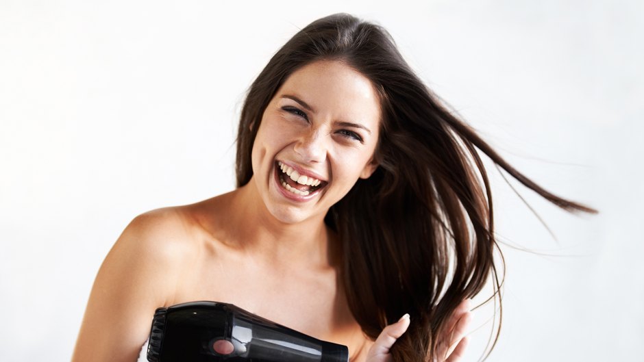 Playful portrait of an attractive young woman blowdrying her hair