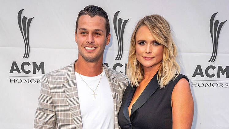 brendan mcloughlin wears a white t shirt underneath a gray and white plaid blazer while miranda lamber wears a sleeveless black blazer mini dress on the 2019 ACM Honors event miranda lambert shouts out husband brendan mcloughlin onstage at her concert